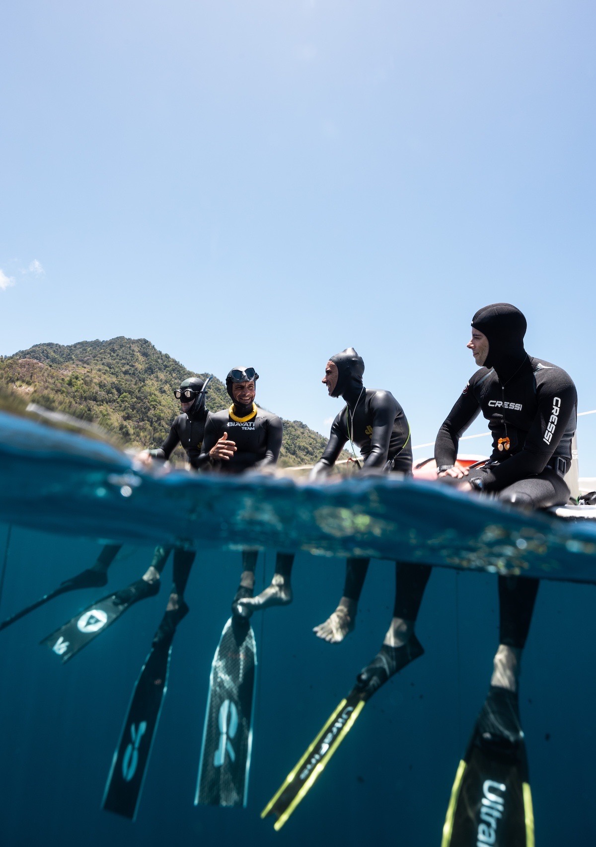 Two divers surfacing together in the bay, the green headland behind them