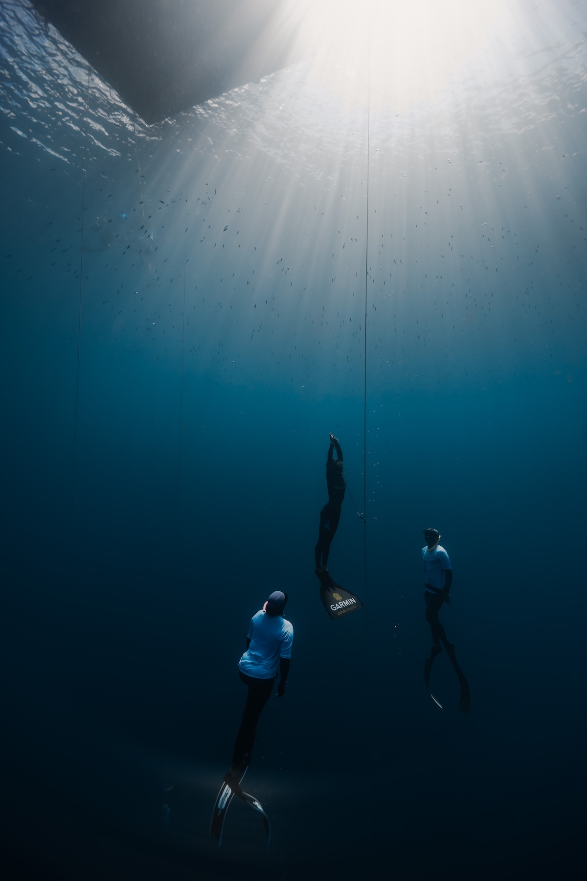 Freediver ascending the line toward the light, flanked by two safety divers