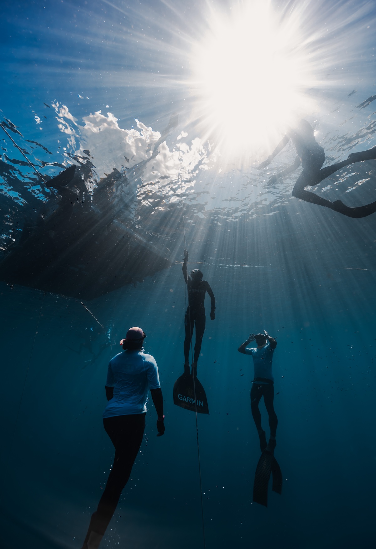 Competitor ascending the mainline toward the sunburst, safety divers alongside