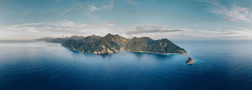 Aerial panorama of Dominica's southern coastline — rainforest mountains dropping into deep blue sea at Scott's Head
