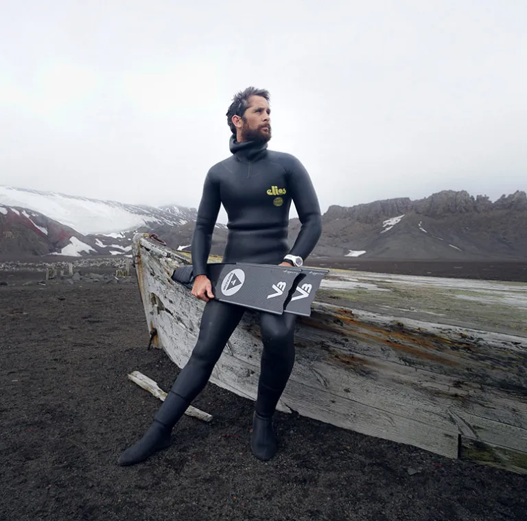 Jonathan Sunnex in his wetsuit holding a carbon monofin, snow-capped mountains behind