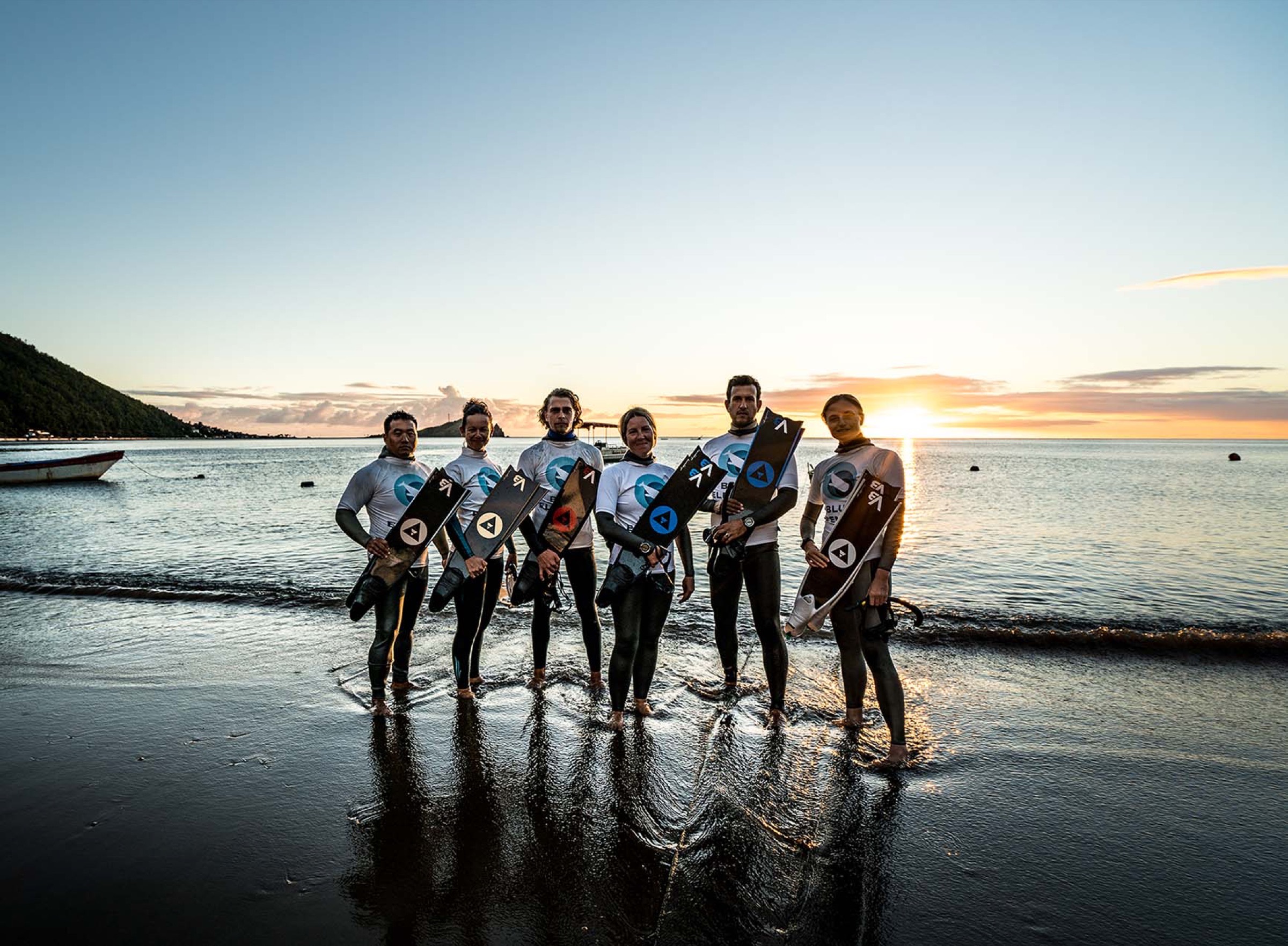 The Blue Element team on the beach at sunset holding monofins
