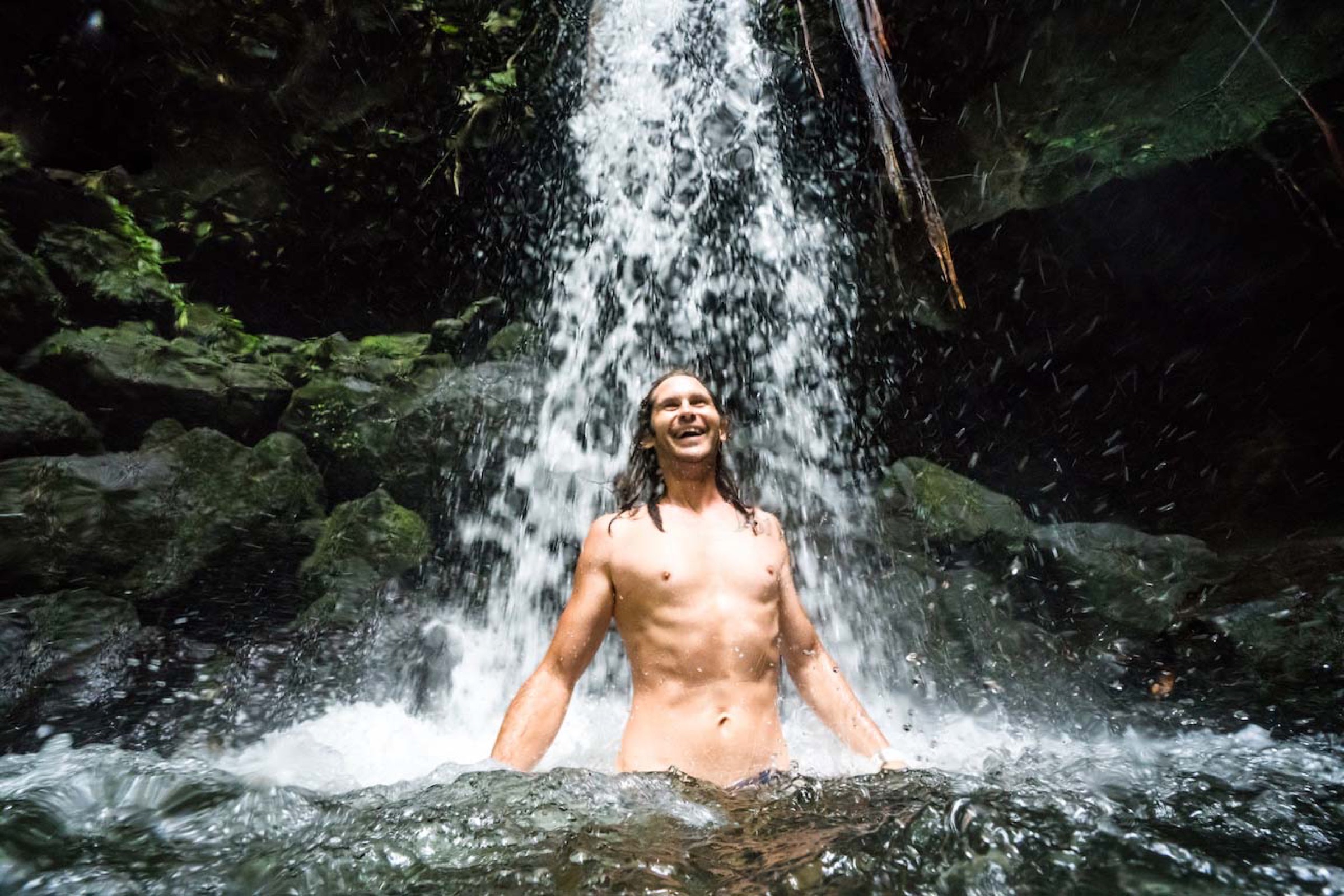 A freediver laughing under a jungle waterfall in Dominica